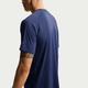 En person ses bagfra og fra siden iført Nike Stride SS Running Top, Herre, Midnight Navy/Reflective Silv. Denne løbetop til mænd har diskrete refleksdetaljer, og personen har en tatovering på højre overarm.