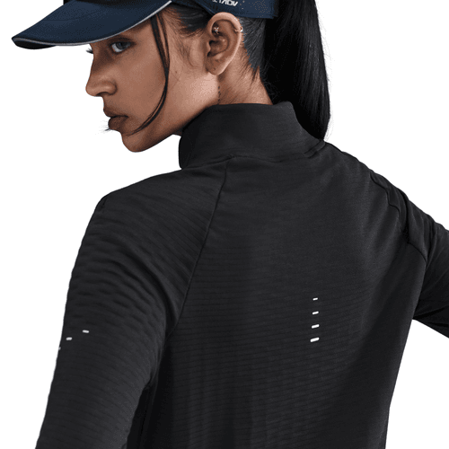 En kvinde ses bagfra iført en sort Nike Therma-FIT Turtle-Neck Running Top med reflekterende sølvfarvede detaljer og synlige ventilationshuller på ærmet og øverst på ryggen, sammen med en marineblå kasket.