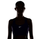 En kvinde iført en lilla Nike High-Support Lightly Lined Sports Bra (Dame, Purple Pulse) med et reflekterende logo står foran en hvid baggrund. Hendes ansigt og krop er stort set i skygge på grund af den bagfra kommende belysning, hvilket fremhæver bh’ens design med høj støtte – ideel til løbetræning eller andre aktiviteter med høj belastning.