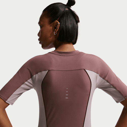 En kvinde ses bagfra iført en tætsiddende Nike Swift Dri-FIT Short-Sleeve Running Top i Tattoo/Lt Violet Ore/Reflective Silver med små reflekterende linjer midt på ryggen. Baggrunden er almindelig hvid.