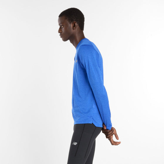 En mand står i profil mod en hvid baggrund iført New Balance Athletics Long Sleeve, Herre, Blue Gemstone Heather og sorte sportsbukser med hænderne samlet bag ryggen.