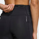 En kvinde kigger væk fra kameraet iført Adidas Adi365 Leggins Dame i sort med en lynlåslomme og "CLIMALWARM" på siden. Hendes venstre hånd hviler bag hendes ryg og fremhæver disse slanke leggins med høj talje.