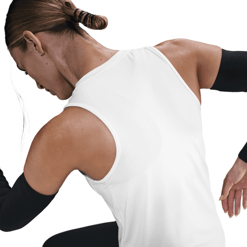 En kvinde med brunt hår i en knold ses bagfra iført Nike Dri-FIT Classic Tank Top til kvinder i hvid/sort med sorte ærmer og løftede og bøjede arme på en almindelig hvid baggrund.