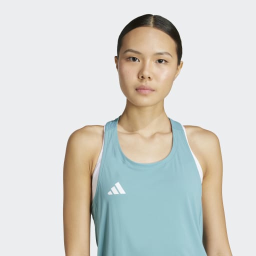 En kvinde med glat mørkt hår bundet tilbage bærer en Adidas Adizero E Tank, Dame, i powtea med et hvidt logo, står på en almindelig lys baggrund og kigger ind i kameraet.