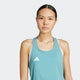 En kvinde med glat mørkt hår bundet tilbage bærer en Adidas Adizero E Tank, Dame, i powtea med et hvidt logo, står på en almindelig lys baggrund og kigger ind i kameraet.