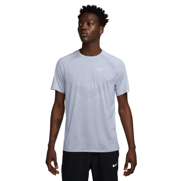 En person iført Nike Dri-FIT ADV Short-Sleeve Running Top, Herre, Ghost/Htr/Reflective Silv og sorte Nike-shorts står lidt til venstre på en almindelig hvid baggrund.