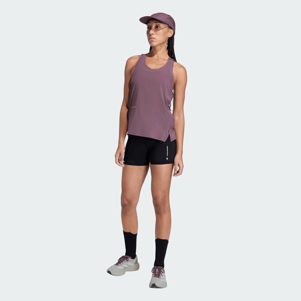 En person iført en Adidas Adi365 Hk Singlet, Dame, Shafig i mauve, med sorte shorts, sorte sokker, grå løbesko og en matchende mauve kasket står på en almindelig lysegrå baggrund.