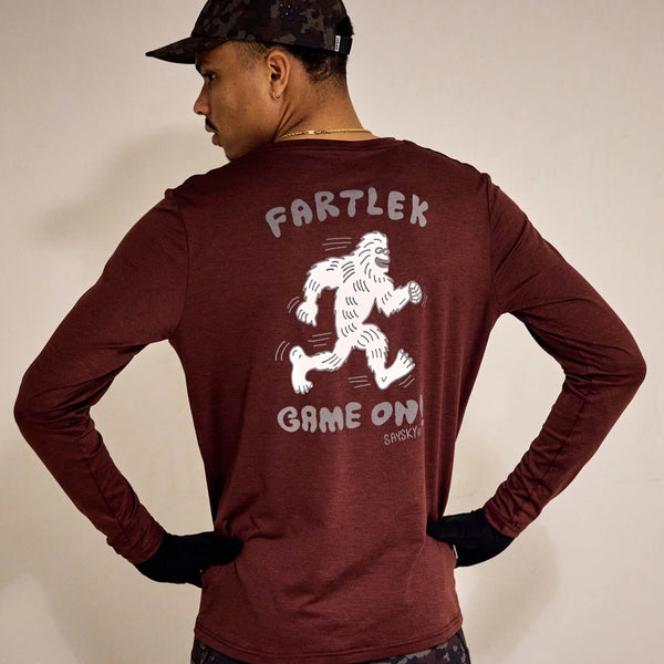 En person, der kigger væk fra kameraet, bærer en rød Saysky Statement Pace Long Sleeve, Herre, med en hvid, løbende yeti og "FARTLEK GAME ON" på ryggen.