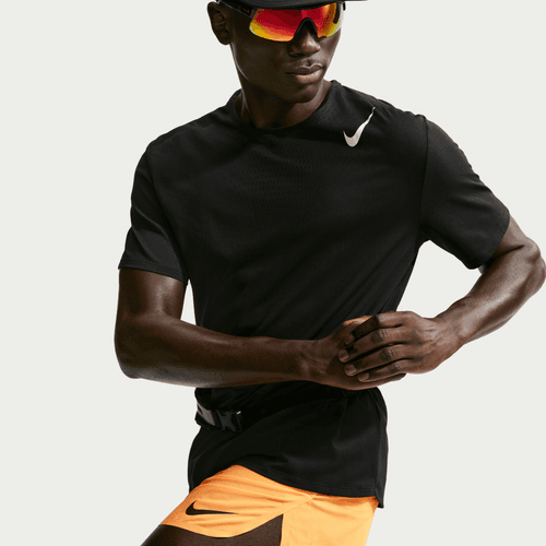 En person er iført en sort Nike t-shirt, AeroSwift 4In Brief-Lined Running Shorts for men i Laser Orange/Black, en sort kasket og reflekterende solbriller og poserer, som om han løber mod en almindelig hvid baggrund.