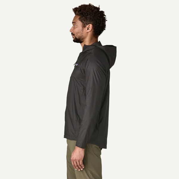 En mand i profil mod venstre iført olivengrønne bukser og en Patagonia Houdini Jacket, Herre, Black w/Black, står på en almindelig hvid baggrund.