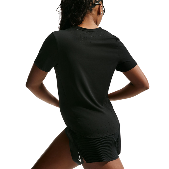 En person står med hænderne i siden, vendt væk fra kameraet, iført Nike Dri-FIT ADV løbetrøje til kvinder i sort/hvid og sorte sportsshorts – svedtransporterende løbetøj, der er designet til at sikre komfort under intense løbeture. Den ensfarvede hvide baggrund fremhæver overkroppen og de øverste ben og giver et klart overblik over denne elegante Nike-løbetrøje til kvinder.