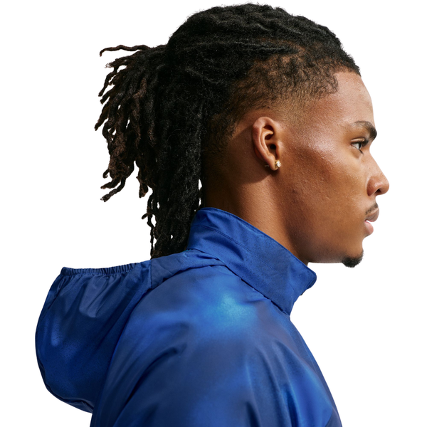 En person med lange, sammenbundne dreadlocks og en ørestik vises i højre profil, iført Nike Miler UV Repel-løbejakken til mænd i farvekombinationen Midnight Navy/Reflective Silver på en hvid baggrund.