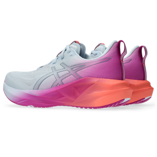 Asics Novablast 5 Dame i Sky/Digital Sakura har lyseblå overdel, pink Asics-logoer, tykke mellemsåler med en gradient fra pink til orange, pink hælkapper og hvide ydersåler.