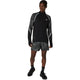 En person er iført Asics Limited Series Lite-Show Ls Top, Herre, Performance Black med geometrisk mønstrede ærmer og matchende shorts, parret med sorte sokker og sportssko, og kigger til siden.