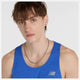En lyshudet person med brunt hår iført en blå Athletics Tank, Herre, Blue Gemstone Heather fra New Balance, pyntet med en sølvkæde og en lille ørering, kigger ind i kameraet mod en almindelig lys baggrund.