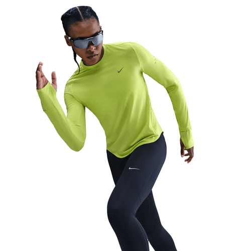 En kvinde i en knaldgul Nike Dri-FIT UV Long-Sleeve Crew-Neck Running Top (Dame, Cyber/Htr/Reflective Silv), sorte leggings og solbriller poserer i en løbestilling mod en hvid baggrund.
