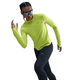 En kvinde i en knaldgul Nike Dri-FIT UV Long-Sleeve Crew-Neck Running Top (Dame, Cyber/Htr/Reflective Silv), sorte leggings og solbriller poserer i en løbestilling mod en hvid baggrund.