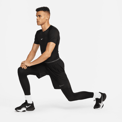 En person i sort Nike-sportstøj og hvide sokker udfører et udfaldsstræk på en hvid baggrund, iført Nike Df Tight Top Ss, Herre, Black/White for optimal komfort under træning.