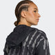 En person med cornrow-fletninger ses i profil mod højre iført Adidas Adi365 Jacket til kvinder i sort/refsil, som har et lysegråt zigzag-mønster på ryggen og skuldrene.