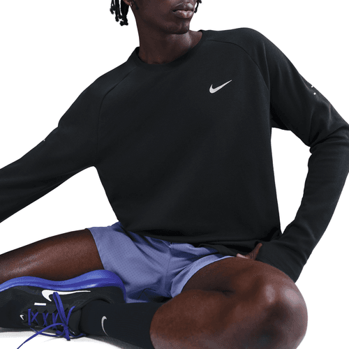 En person sidder med det ene knæ oppe iført en sort Nike Dri-FIT Running Waffle Crew til mænd (Black/Reflective Silv), lyslilla sportsshorts, sorte sokker og sorte sneakers med lilla detaljer. Ansigtet er delvist ude af billedet.