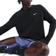 En person sidder med det ene knæ oppe iført en sort Nike Dri-FIT Running Waffle Crew til mænd (Black/Reflective Silv), lyslilla sportsshorts, sorte sokker og sorte sneakers med lilla detaljer. Ansigtet er delvist ude af billedet.