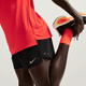 En person i orange skjorte, orange sokker og Nike Stride 5" Brief-Lined Running Shorts til mænd (Black/Reflective Silv) strækker sig ved at holde den ene fod tilbage. Kun underkroppen og benene vises; det fugttransporterende stof holder dem kølige.