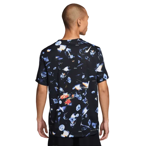 En person med kort hår står med ryggen til kameraet iført Nike Aeroswift Aop Ss Running T-Shirt til mænd i sort/laser orange med et levende, abstrakt mønster. Baggrunden er almindelig hvid.