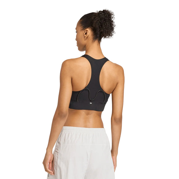 En kvinde ses bagfra iført en Adidas Adi365 Pkt Bra til kvinder i sorte og hvide sportsshorts, stående mod en almindelig lys baggrund.