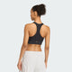En kvinde ses bagfra iført en Adidas Adi365 Pkt Bra til kvinder i sorte og hvide sportsshorts, stående mod en almindelig lys baggrund.