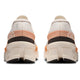 Et par On Cloudmonster 2 dame-sneakers i Ivory/Tangerine, set bagfra, viser en blanding af hvid, fersken og sort med tykke segmenterede Helion-superskumsåler og "ON"-logoet synligt på hver hæl.