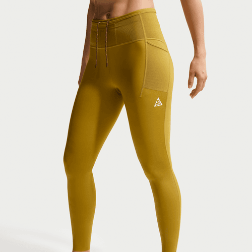 En person iført Nike ACG 7/8 Running Tights til kvinder i Peat Moss/Ironstone/Summit White, med sidelomme og lille trekantet logo på låret, vist fra midt på torsoen til anklen mod en ensfarvet baggrund.