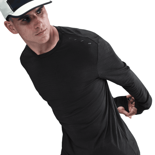 En person strækker sin venstre arm bag ryggen mod en hvid baggrund, mens han er iført en sort Nike Dri-FIT ADV Wool Long-Sleeve Running Top til mænd og en sort-hvid kasket.