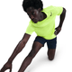 En person i en lys Volt/Black Nike Dri-FIT ADV Short-Sleeve Running Top, Herre og marineblå shorts strækker sig med det ene knæ på jorden og den ene arm strakt frem.