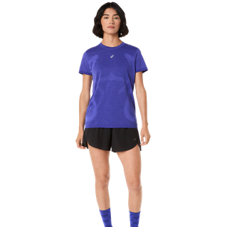 En person iført en lilla kortærmet t-shirt, Asics Metarun Split Shorts Dame i Performance Black og lilla sokker står på en almindelig lys baggrund.