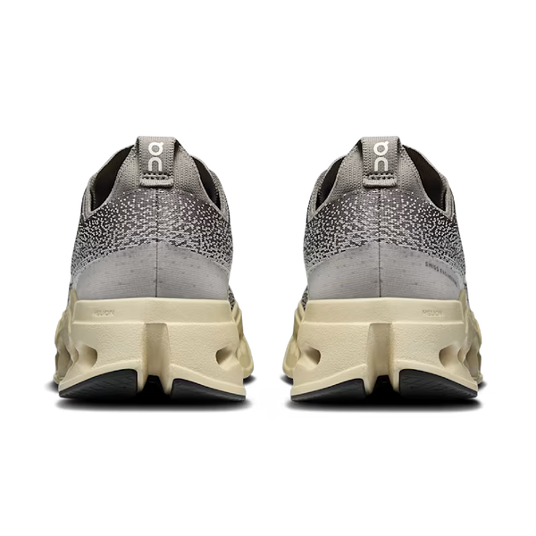 Et par On Cloudsurfer Max, Herre, Asphalt/Ice løbesko set bagfra med tekstureret overdel, On-mærkede trækflige og tykke beige såler med geometriske riller for maksimal komfort.