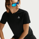 En person med lysebrunt hår og blå reflekterende solbriller er iført en sort Nike ACG kortærmet løbetop (Dame, Black/Summit White) med et lille hvidt trekantet logo, der sidder på en almindelig lys baggrund.