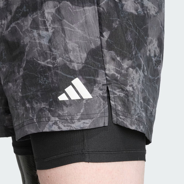 Nærbillede af en mands overben iført Adidas Otr Sd 2In1 M shorts i Grefou/Black, lagt over sorte kompressionsshorts - ideelle 2-i-1 træningsshorts til herrer.