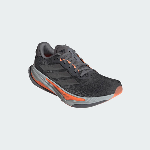 Adidas Supernova Prima 2 herre løbesko i Grefou/Ironmt/Luor har sorte og grå toner med orange detaljer, snørelukning og de karakteristiske tre striber, der vises på en almindelig lys baggrund.
