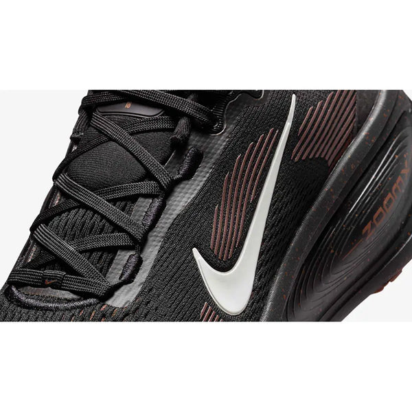 Nærbillede af Nike Vomero 18 Herre løbesko i Black/Ironstone-Velvet Brown med hvid Swoosh, sorte snørebånd, tekstureret stof, "Zoom" på sålen med responsiv ZoomX-skum og brune detaljer.
