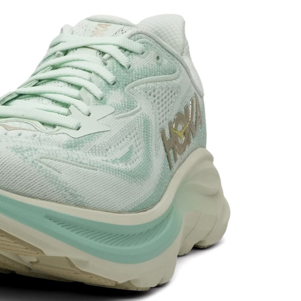 Et nærbillede af Hoka Clifton 10 dame løbesko i Sea Glass/Jadeite med tykke polstrede såler og HOKA-logoet på siden mod en hvid baggrund.