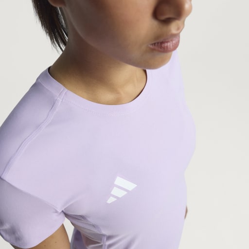 En kvinde ses fra skuldrene og opefter iført Adidas Adizero E Tee, Dame in Powplu. Billedet fremhæver den ultralette pasform og viser et lille hvidt logo på brystet, hvor kun en del af hendes ansigt er synligt.