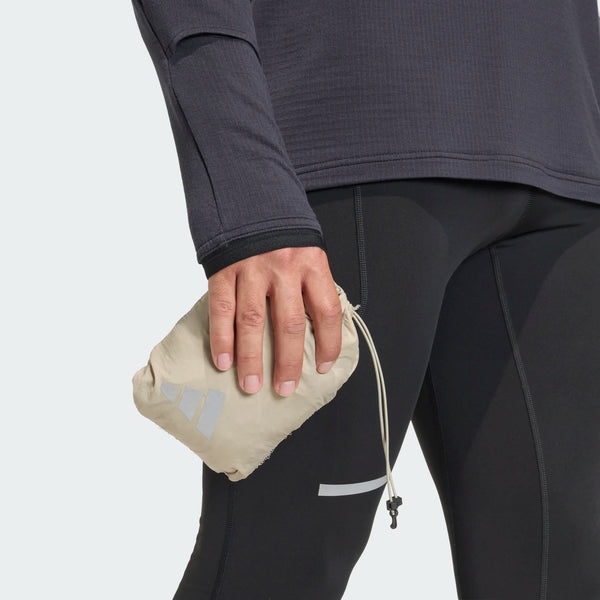 Klædt i sorte leggings og en mørk langærmet top holder en person en lille beige pose med et reflekterende logo - ideel til at kombinere med Adidas Adi365 High-Vis Jacket, Herre, Woca - i venstre hånd i lårhøjde.