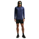 En person med langt hår, iført solbriller, en marineblå Nike Dri-FIT ADV langærmet løbetrøje til mænd i farvekombinationen Midnight Navy/Reflective Silver, sorte shorts, sorte løbesko og et smartwatch, står med ansigtet vendt fremad foran en hvid baggrund.