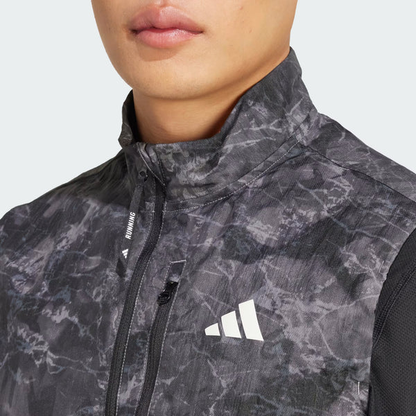 Nærbillede af en person iført Adidas Otr Sd Vest M til mænd i Grey Four/Black med lynlås og logo på brystet. Den svedtransporterende vest er ideel til aktive dage. Ansigt delvist synligt, ensfarvet baggrund.