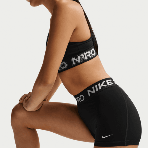 En person i sorte Nike Mid-Rise 3 Biker Shorts, Dame, Black/White knæler med det ene knæ oppe og fremhæver fede Nike-logoer. Billedet fokuserer på det sporty look med mærkets signatur træningstøj damer på torso og overben.