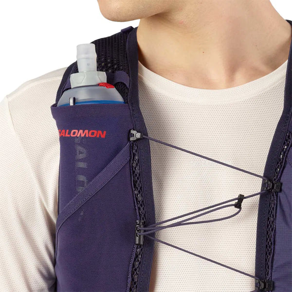 En person i hvid skjorte og en Salomon Active Skin 4 Set løbevest i Maritime Blue/Astral Aura/Haute Red med en synlig soft water-flaske i forlommen; elastiske brystsnore gør den ideel til trailløb.