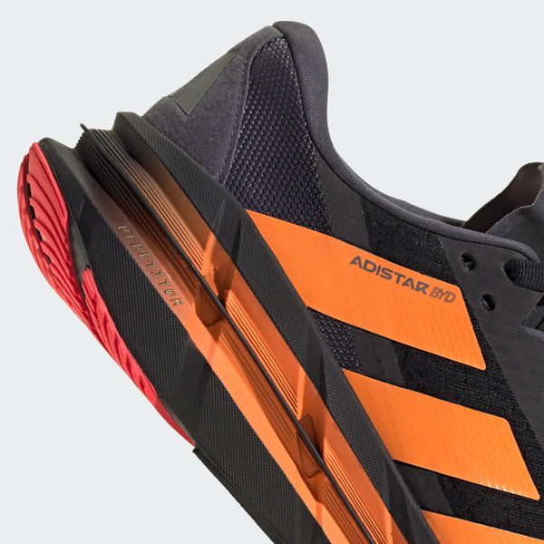 Nærbillede af Adidas Adistar Byd løbesko til herrer i Cblack/Luor/Auon, der viser REPETITOR+ mellemsålen for maksimal komfort, Adistar BYD-branding på siden og en rød/sort ydersål.