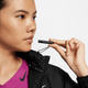 En person iført en sort Nike Therma-FIT løbejakke, Dame, Black/Reflective Silv og en lilla skjorte holder en sort fløjte ved munden og kigger til siden.