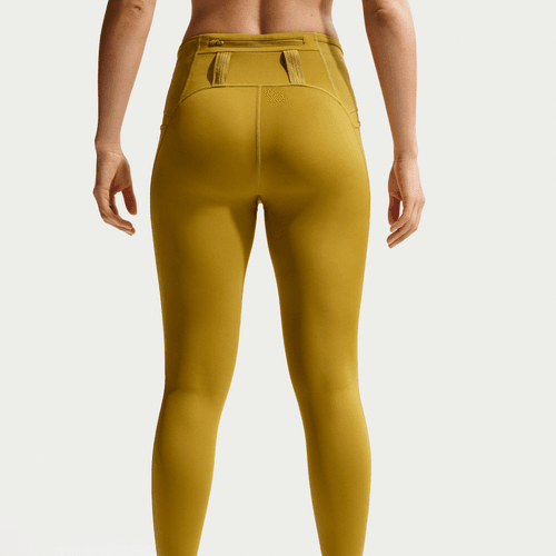 En person kigger væk fra kameraet iført Nike ACG 7/8 Running Tights i Peat Moss/Ironstone/Summit White. Bagsiden viser det tætsiddende design og den detaljerede linning på disse tights til kvinder.