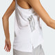 En kvinde ses bagfra iført den hvide Adidas Iconic Tank Top, Dame, med grå rygstriber. Den ene arm er bøjet, mens den anden er afslappet. Den ensfarvede, lyse baggrund fremhæver dette stilfulde træningstop dame.